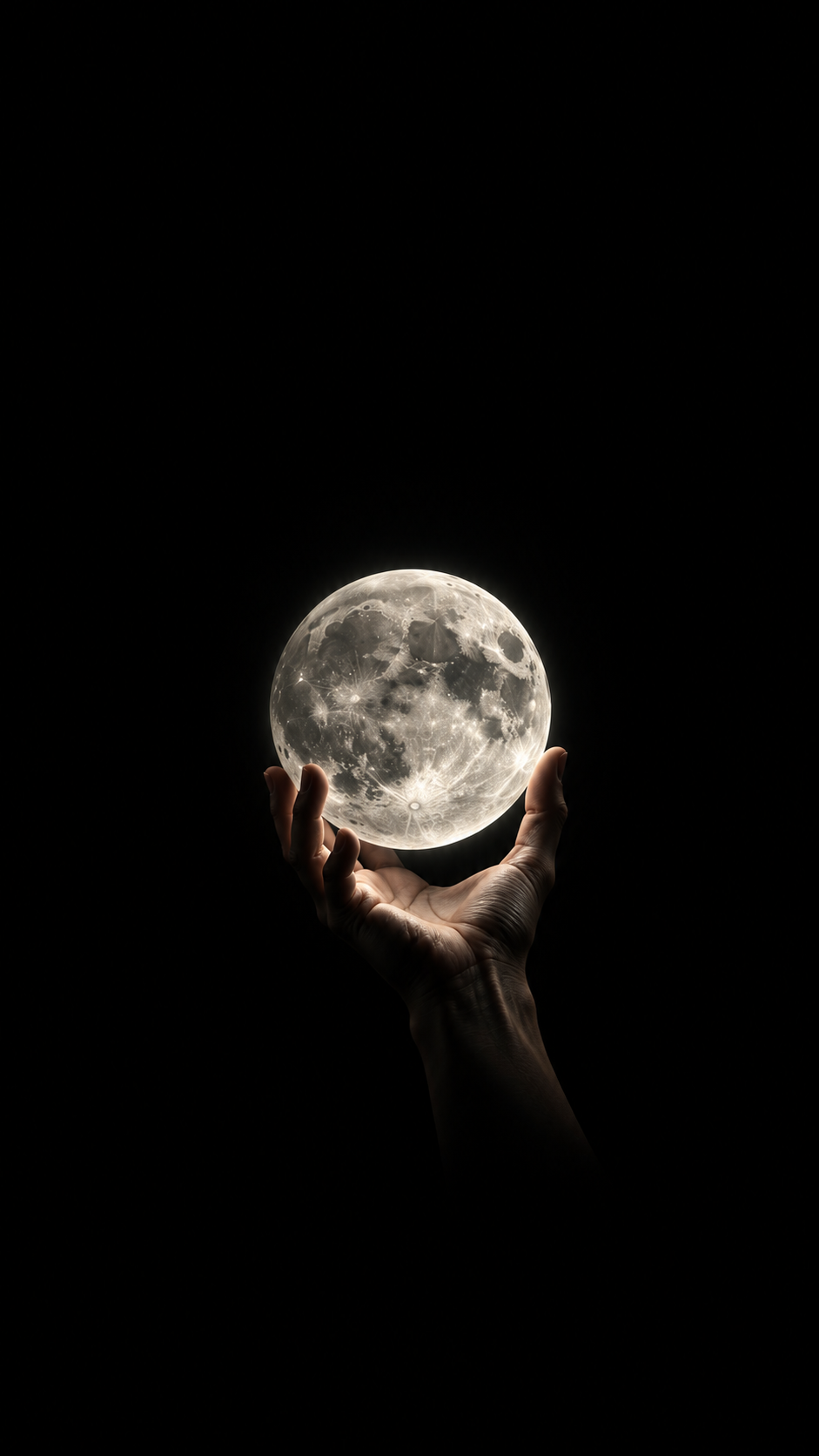 A human hand gently holding a detailed luminous full moon against a deep black background.