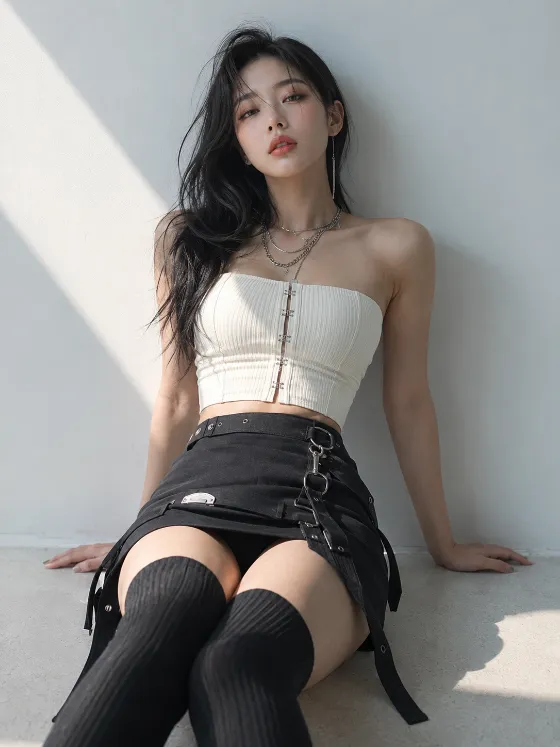 Low-angle fashion portrait of an adult woman in black-and-ivory styling with thigh-high socks and silver jewelry beside diagonal sunlight.