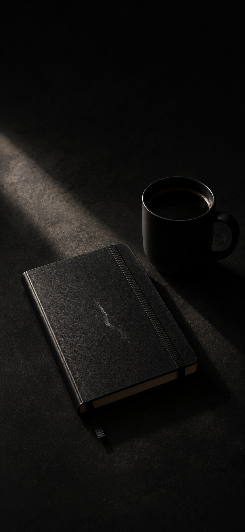 Minimal dark wallpaper of a black notebook and black coffee mug on a charcoal tabletop with soft diagonal light.