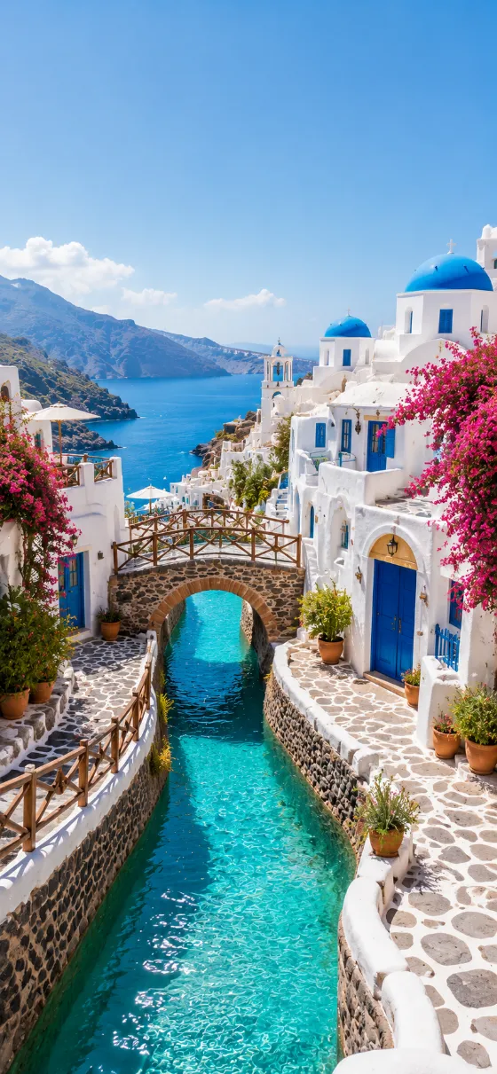 White Mediterranean village with blue domes, turquoise canal, flowers, arched bridge, sea, and mountains.