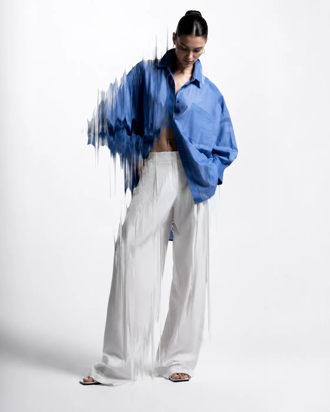 Studio fashion portrait of a woman in a blue oversized shirt and white trousers with a glitch-like distortion effect.