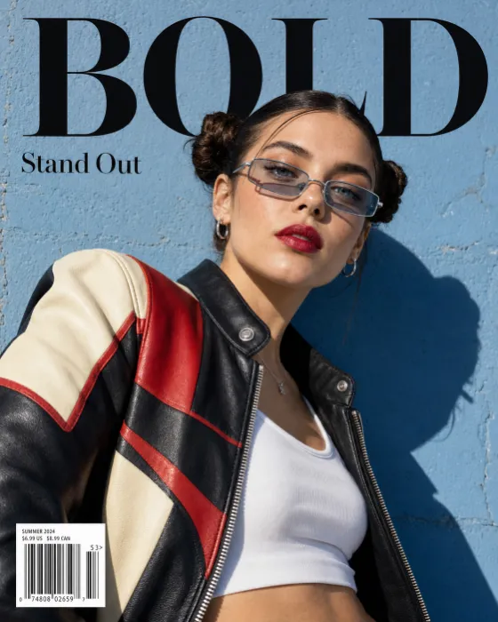 Close diagonal fashion portrait with a color-block leather jacket, narrow metallic glasses, bold typography, and a powder-blue wall.