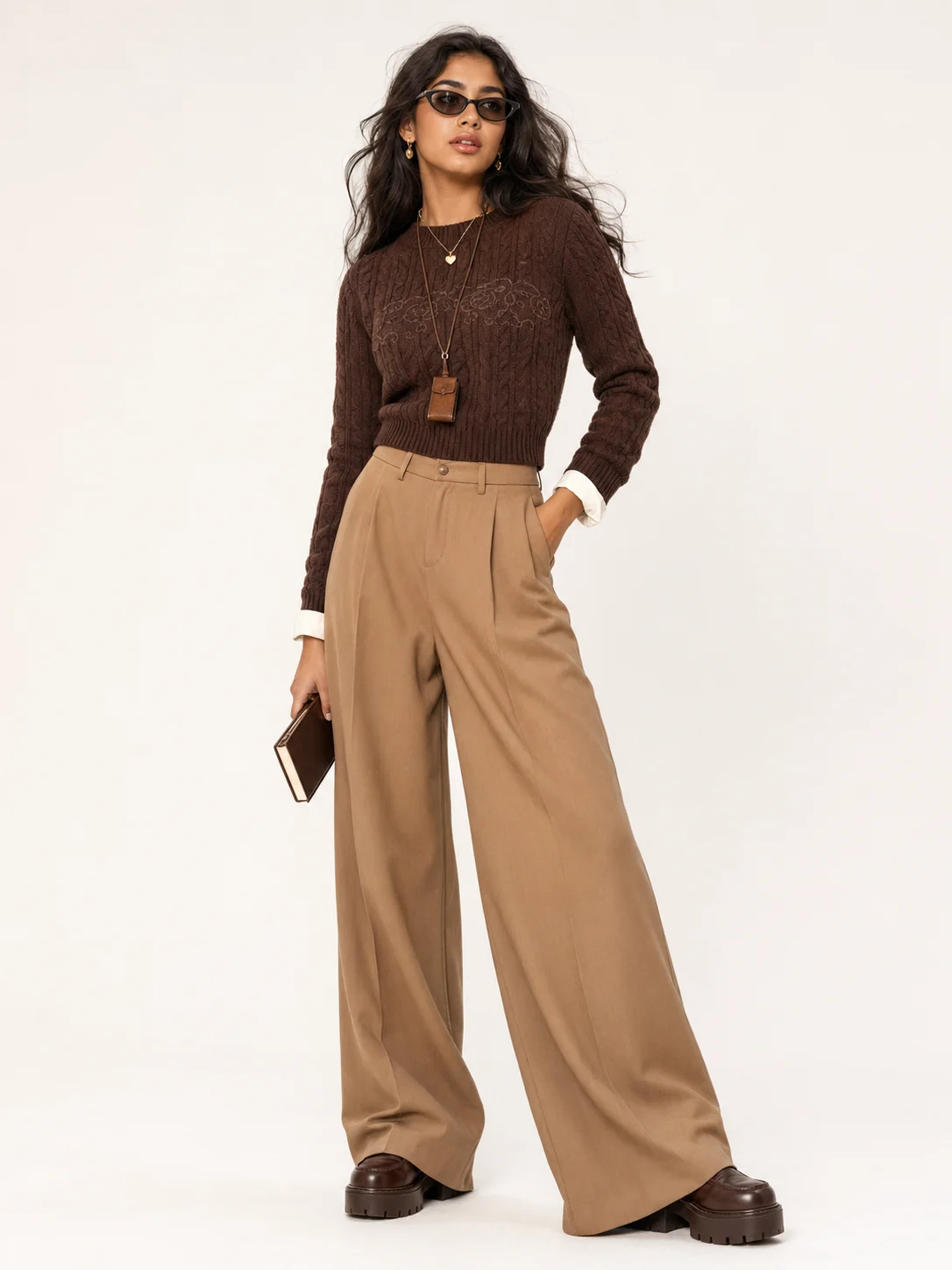 Studio fashion look with chocolate knitwear, camel wide-leg trousers, layered necklaces, dark glasses and chunky brown platform loafers.