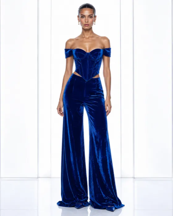 Full-body model in a cobalt blue velvet off-shoulder corset and matching wide-leg trousers in a white studio.