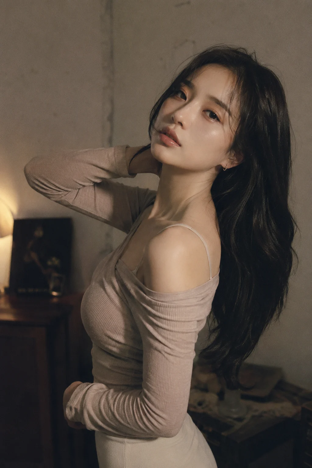 An elegant Korean woman with long dark hair, wearing an off-shoulder ribbed top, posing sensually in a dimly lit room with soft, warm lighting.