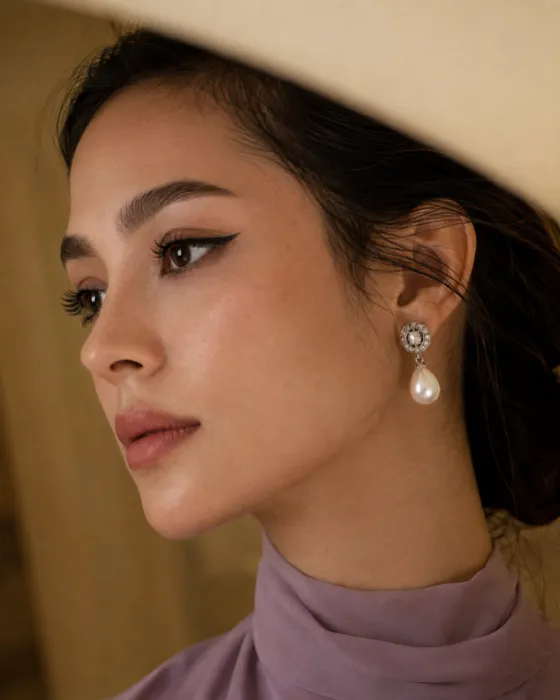 Elegant fashion profile of one woman wearing winged eyeliner, a muted lavender neckline, and a silver-toned pearl drop earring.