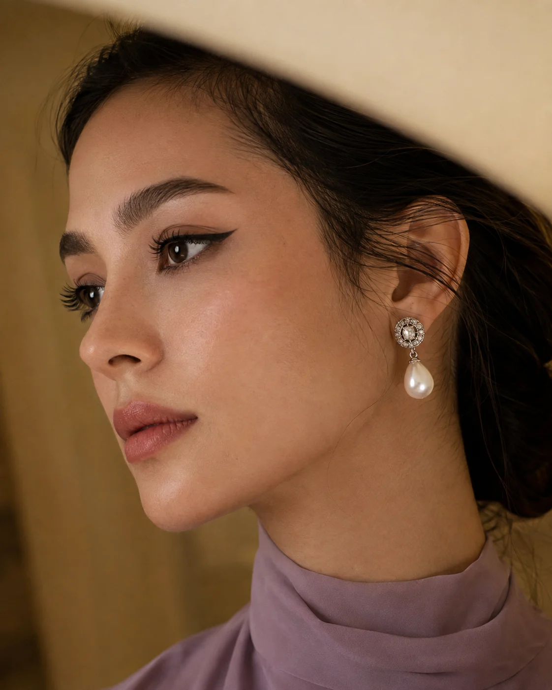 Elegant fashion profile of one woman wearing winged eyeliner, a muted lavender neckline, and a silver-toned pearl drop earring.