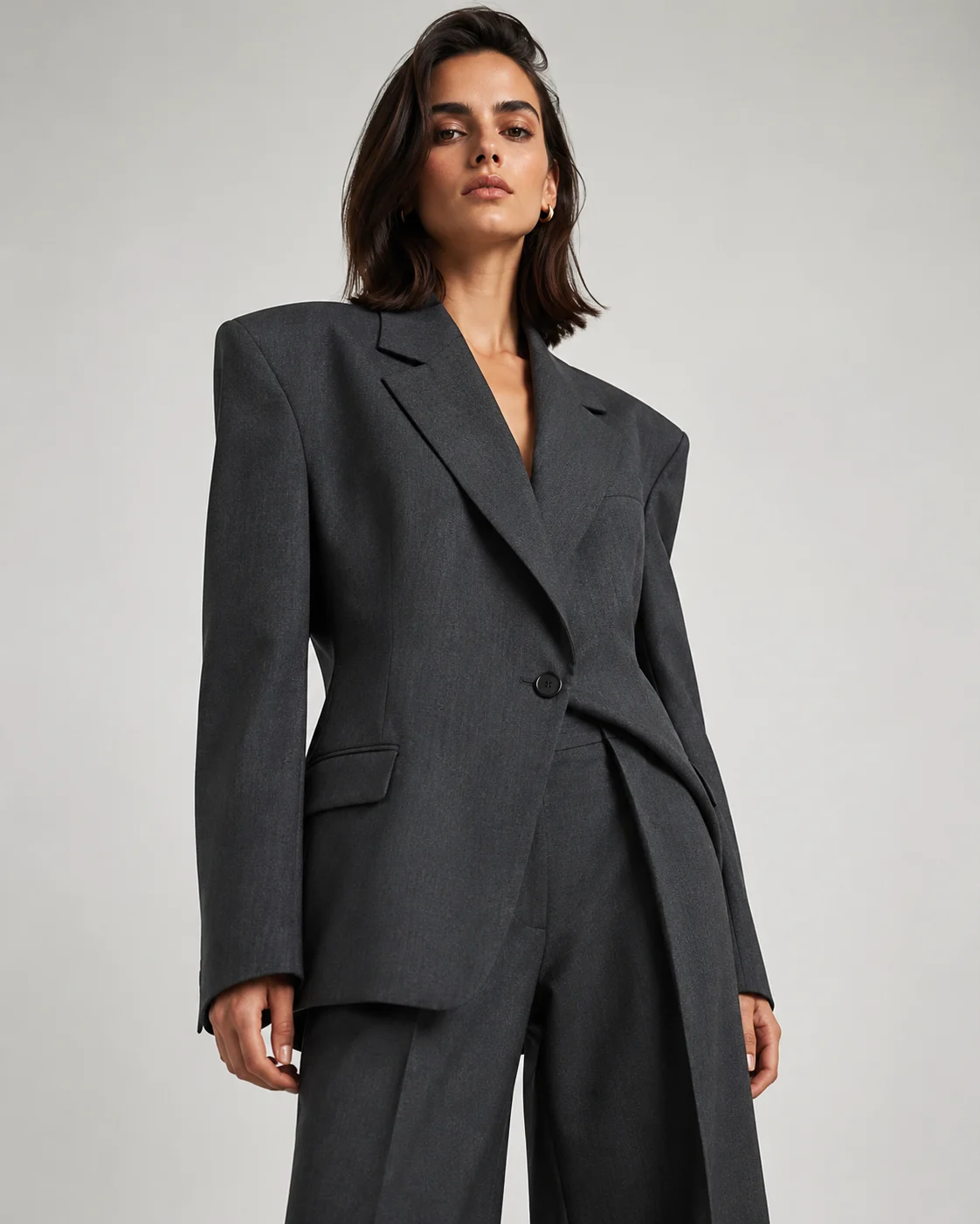Adult model in a charcoal gray oversized tailored suit, highlighting the blazer and wide-leg trousers in a fashion editorial.