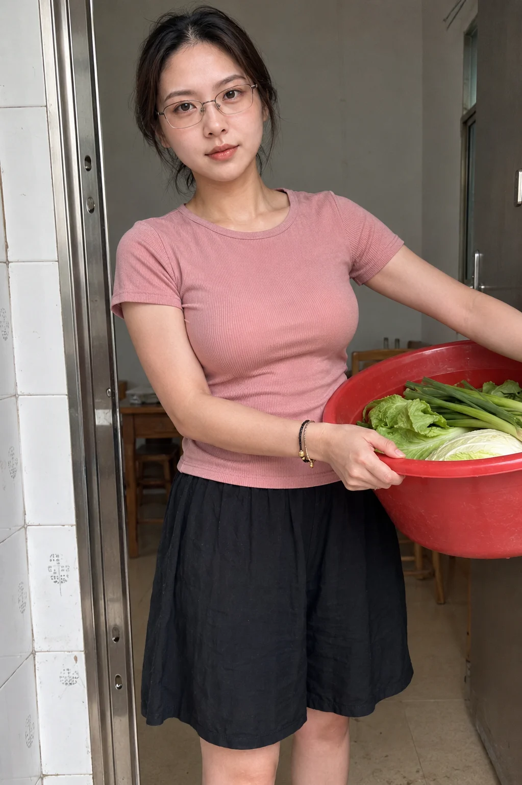 A young woman wearing glasses and a pink t-shirt stands in a doorway, holding a large red basin filled with green leafy vegetables.