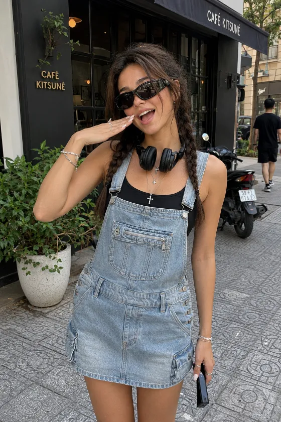 Urban streetwear portrait with braided hair, sunglasses, black tank top, and light-wash denim overall skirt