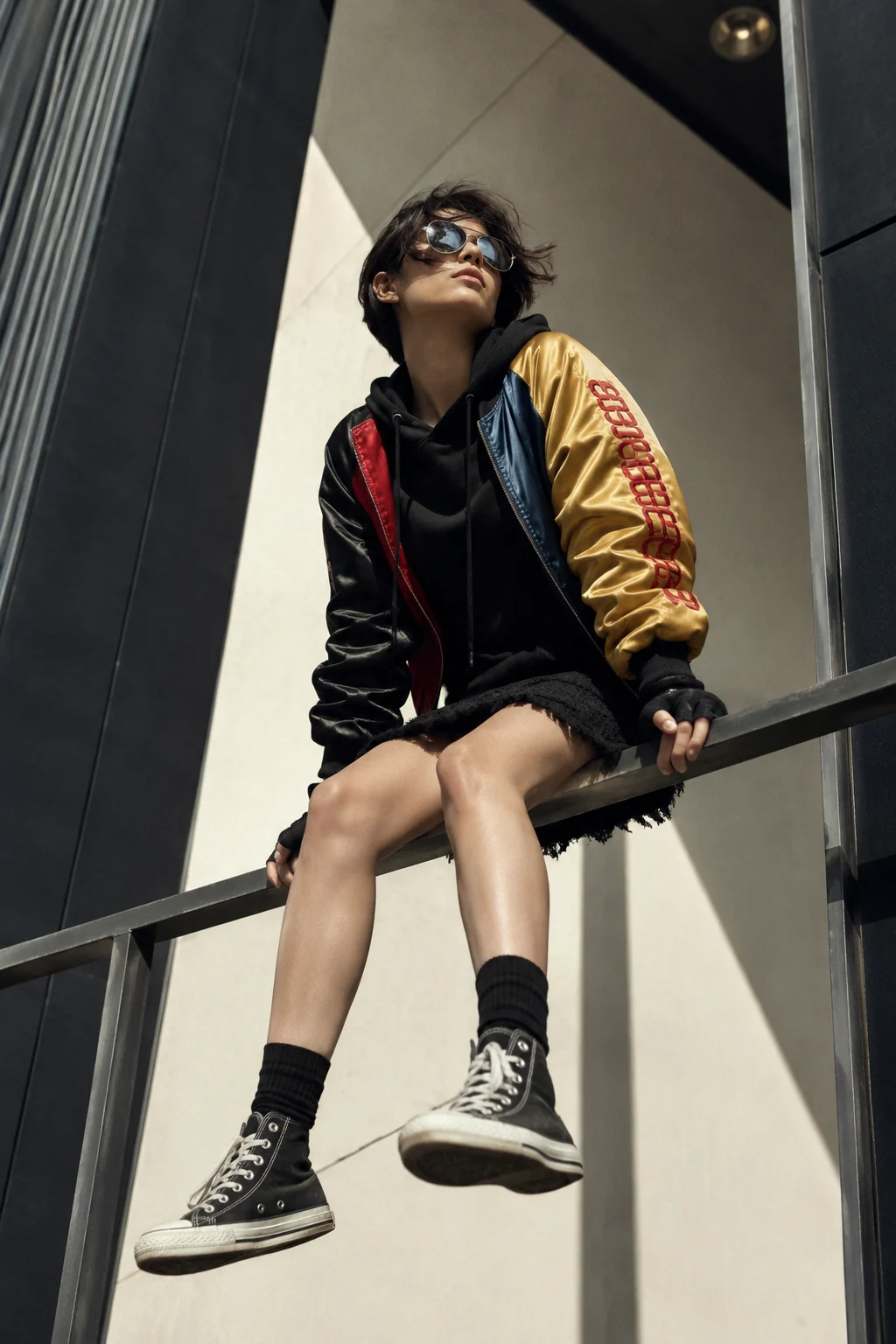 Low-angle editorial portrait of a streetwear subject seated on a railing in a modern geometric interior.
