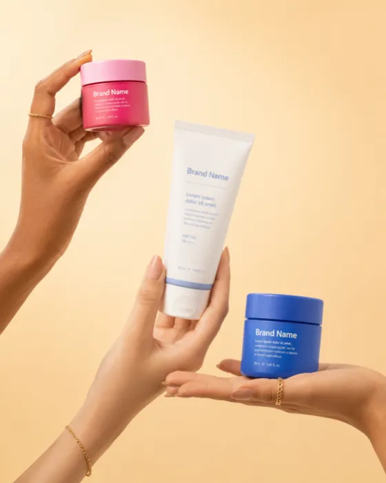 Luxury cosmetic products elegantly presented by graceful hands against a warm minimalist studio background.