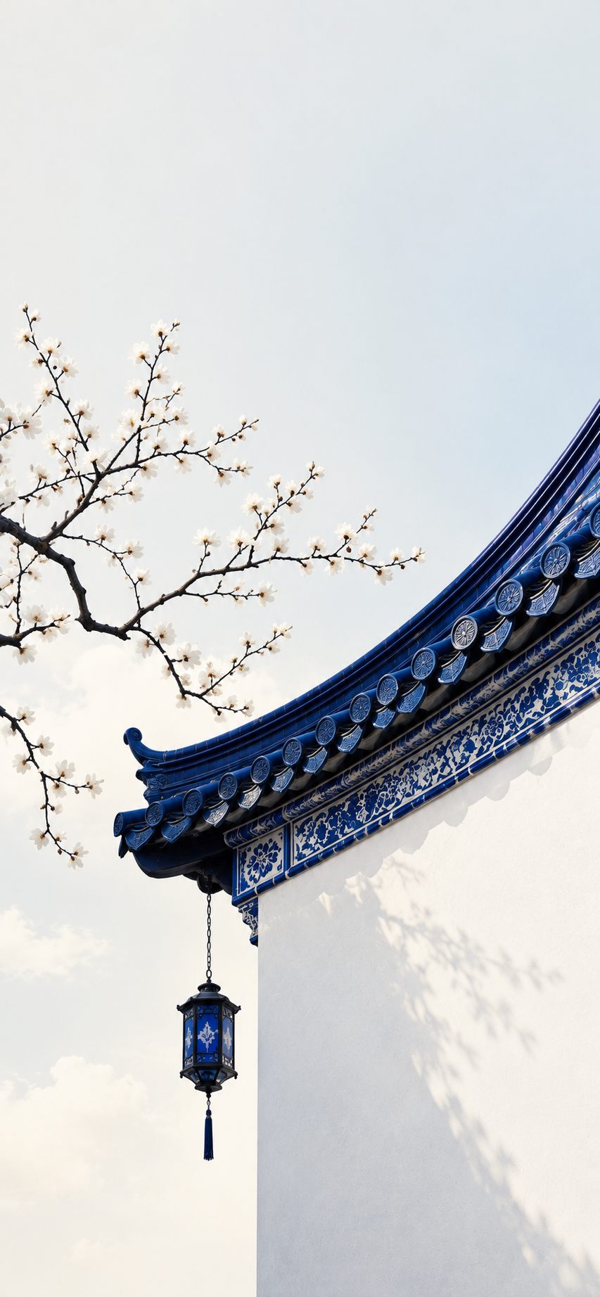 Traditional blue ceramic roof with a hanging lantern against a white wall and flowering branches.