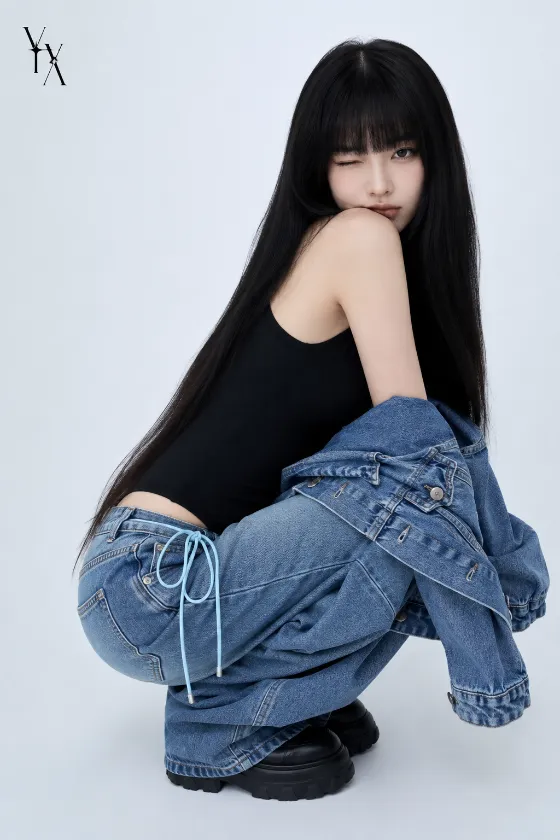 Fashion subject crouching in a fitted black sleeveless top, oversized blue jeans, denim jacket, and black platform shoes