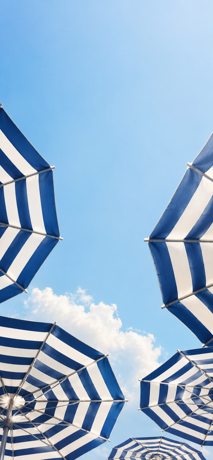 Blue and white striped beach umbrellas viewed from below against a clear summer sky.