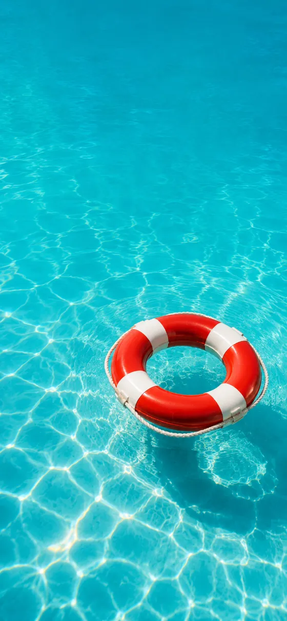 A red and white lifebuoy floating on crystal-clear turquoise pool water under bright sunlight with soft ripples.