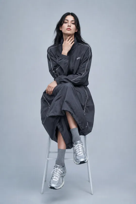 Centered seated fashion portrait in oversized gray technical sportswear and silver sneakers.