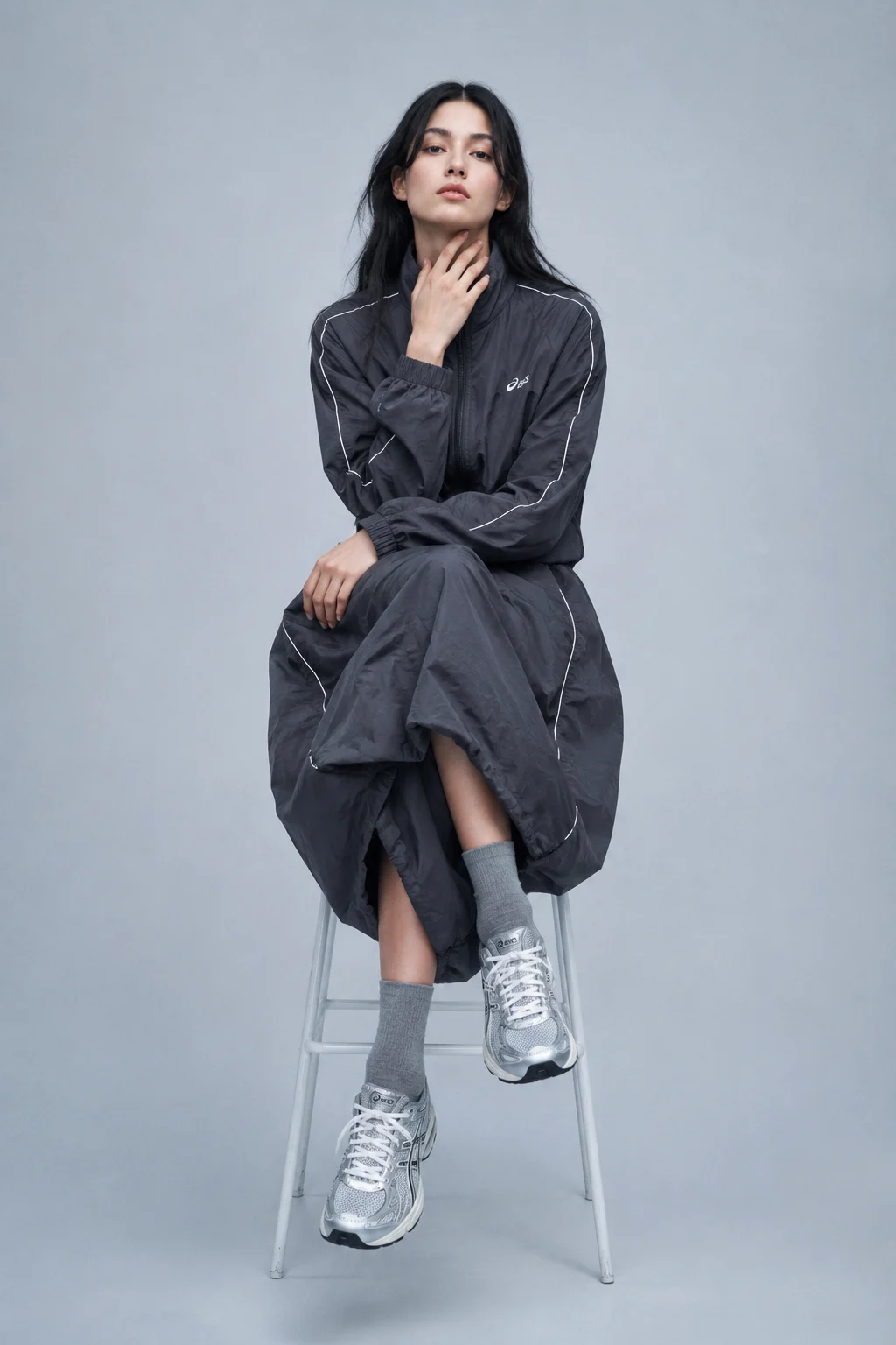 Centered seated fashion portrait in oversized gray technical sportswear and silver sneakers.