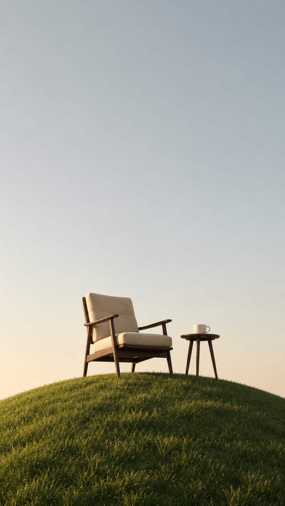 Minimal lounge chair and small side table with a cup on a green hill beneath a vast empty sky.