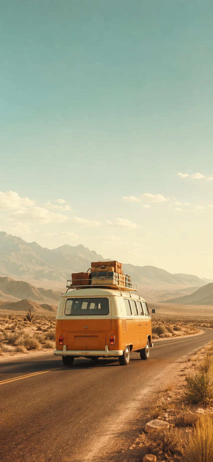 Orange vintage van with roof luggage driving on a desert road toward distant mountains.