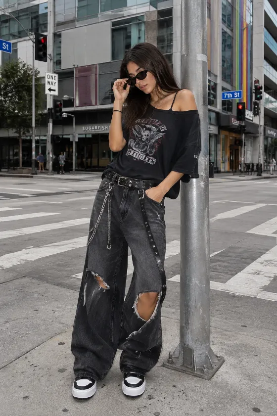 Full-body urban streetwear portrait with oversized black graphic top and distressed wide-leg jeans