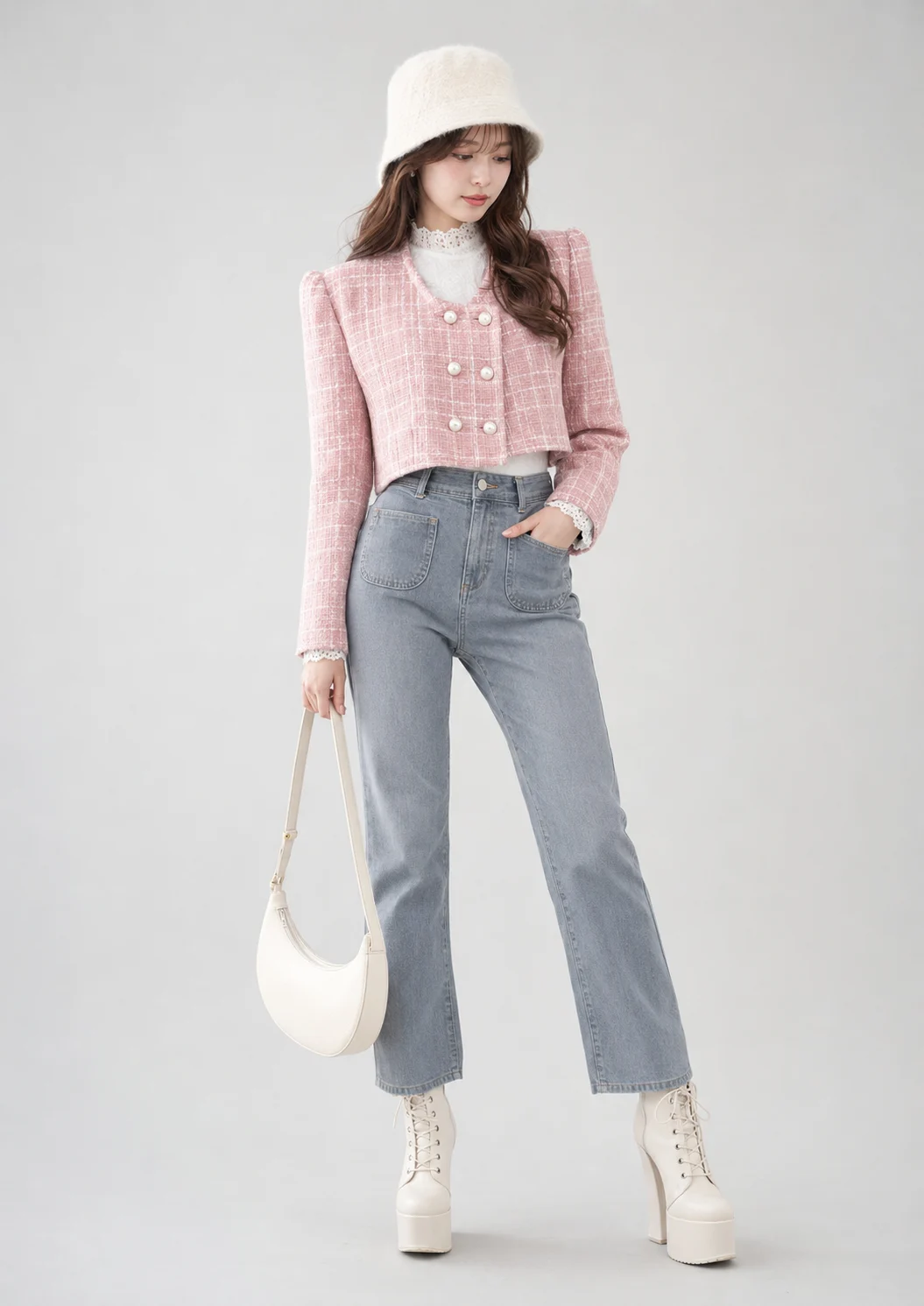 Woman posing in a pale studio wearing a pink tweed jacket, gray jeans, fuzzy ivory hat, cream handbag and tall ivory lace-up platform boots.