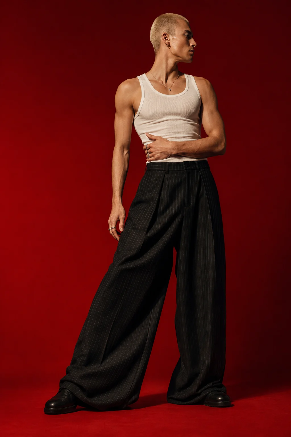 Minimal menswear editorial with white tank, black pinstripe wide-leg trousers, and red backdrop.
