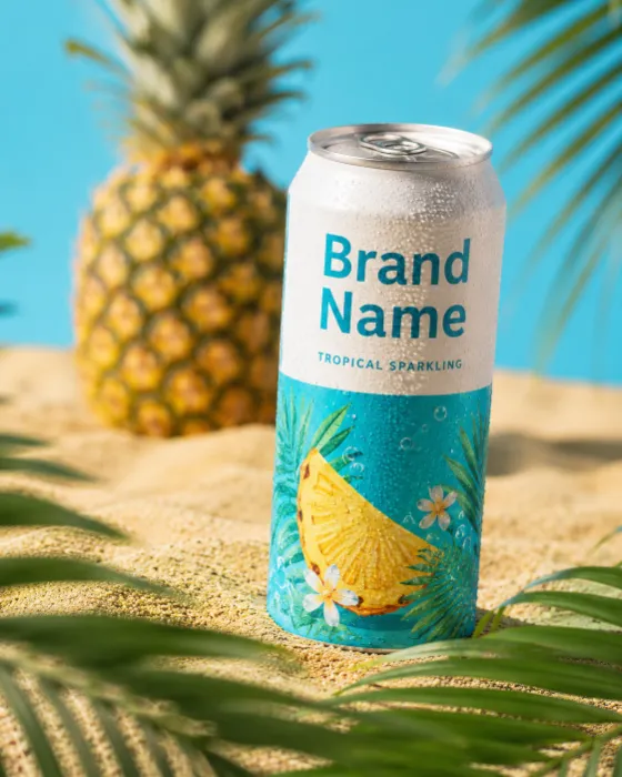 Commercial tropical beverage can photographed in sand with palm leaves and pineapple background.
