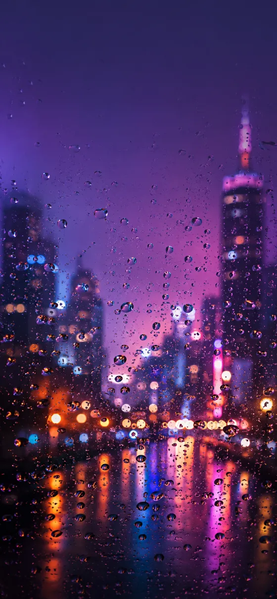 Purple raindrops on wet glass with a blurred neon city background and soft bokeh lights.