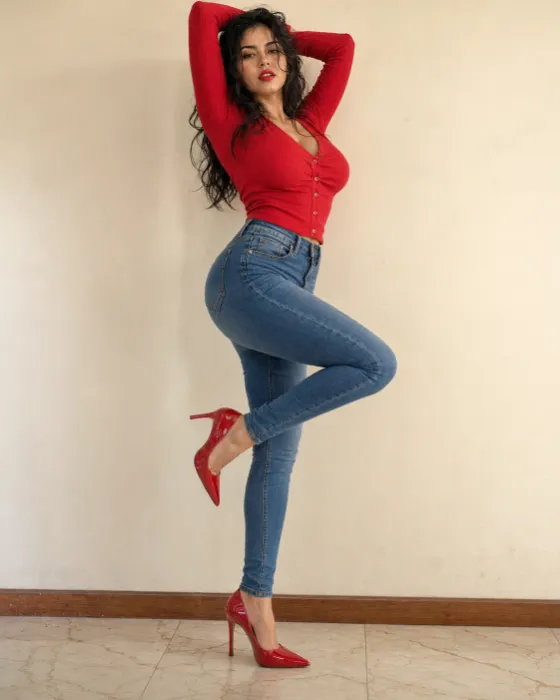Full-body indoor fashion pose with red ribbed top, skinny jeans, and matching red pointed stiletto heels.