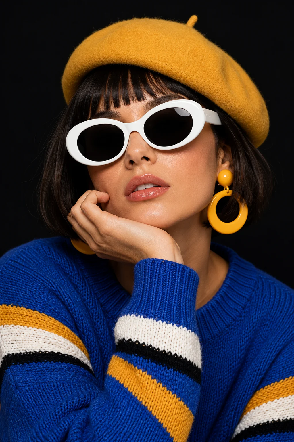 Close-up editorial portrait of a fashion subject wearing a yellow beret, oversized white sunglasses, and a colorful knit sweater against a dark background.