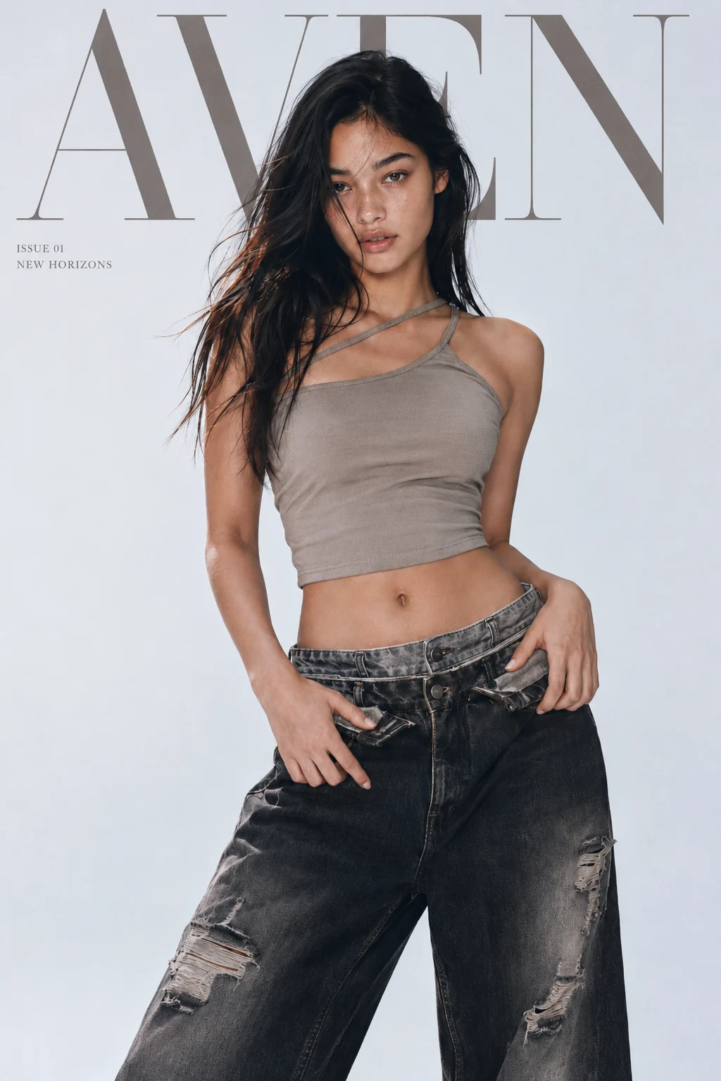 Woman in a taupe asymmetric crop top and distressed charcoal jeans standing under large serif masthead lettering in a pale studio.