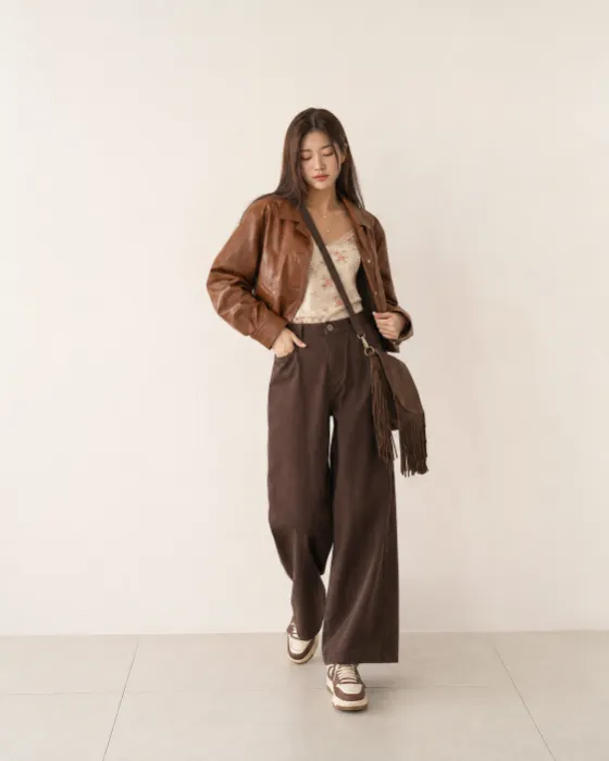 Full-body brown fashion look with a cropped leather jacket, floral ivory camisole, wide-leg trousers and a fringed crossbody bag.