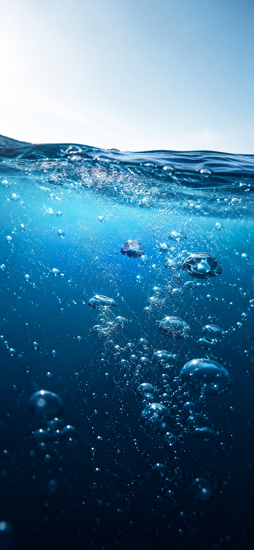 Vertical underwater wallpaper showing a bright waterline above deep blue water filled with reflective air bubbles.