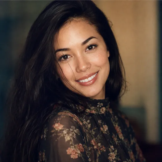 Warm vintage-style fashion close-up of a smiling model in a dark floral blouse with soft bokeh and analog grain.