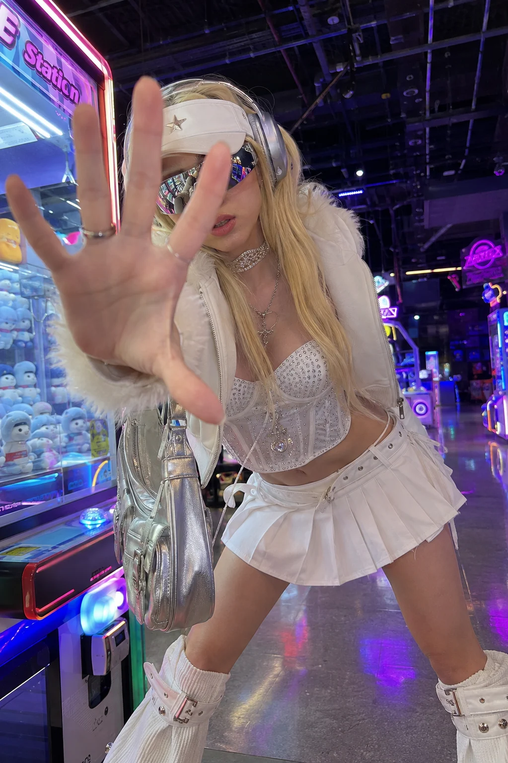 White futuristic Y2K streetwear outfit in a neon arcade with metallic accessories