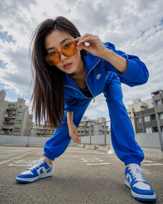 Dynamic low-angle editorial fashion portrait with blue sportswear and oversized amber sunglasses.