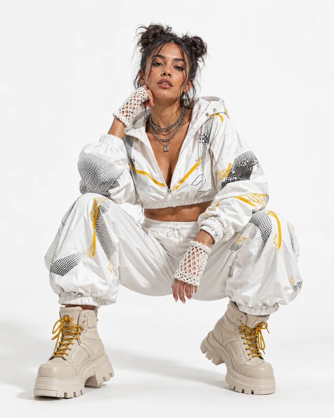 Fashion subject wearing a white printed technical tracksuit with mustard accents, chunky boots, fingerless gloves, and chain necklaces in a clean studio portrait.
